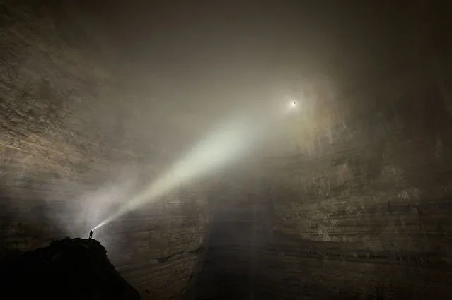 Suspended on a thin rope, engulfed in cloud and lost in time, a tiny figure is dwarfed by the sheer size on a monumental scale of Cloud Ladder Hall. The beam of light cast by anothers head torch pierces the fog yet illuminates nothing. This naturally formed room is so large it has its own weather system going. (Photo by Robbie Shone/Caters News/ImagineChina)