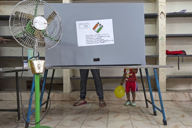 A child holding a balloon stands next to an adult casting his vote at a polling station during the first round of a national election, in Chennai, India, April 19, 2024. (Photo by Altaf Qadri/AP Photo)