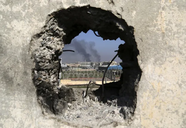 Smoke rises from government complex, seen through a hole in a wall that made by Iraqi forces to fire their weapons, as Iraqi security forces advance during fighting against Islamic State militants in western Mosul, Iraq, Tuesday, March 7, 2017. U.S.-backed Iraqi forces were fighting their way through a government complex in the heart of western Mosul after storming the buildings in an overnight raid, and were facing fierce counterattacks Tuesday from the Islamic State group. (Photo by Khalid Mohammed/AP Photo)