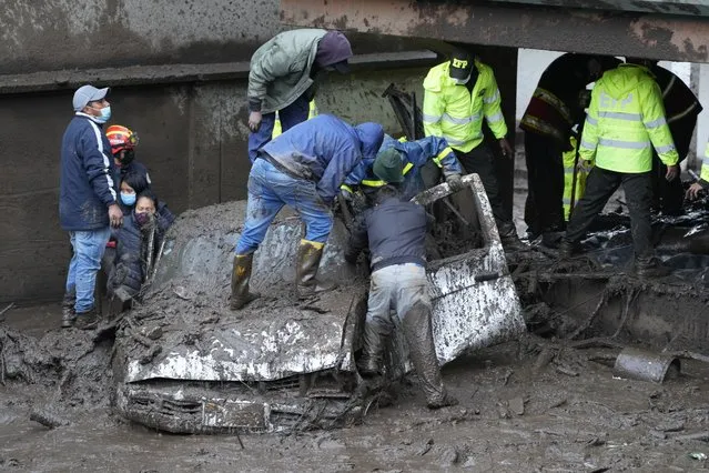 Residents and rescue workers search for people inside a car after a rain-weakened hillside collapsed and brought waves of mud over La Gasca area of Quito, Ecuador, Tuesday, February 1, 2022. (Photo by Dolores Ochoa/AP Photo)