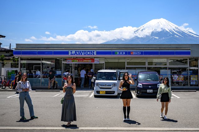 Tourists pose in front of a convenience store with Mount Fuji on May 3, 2024, before a huge black barrier which will be installed to block Mount Fuji from view, in the town of Fujikawaguchiko, Yamanashi prefecture. (Photo by Philip Fong/AFP Photo)
