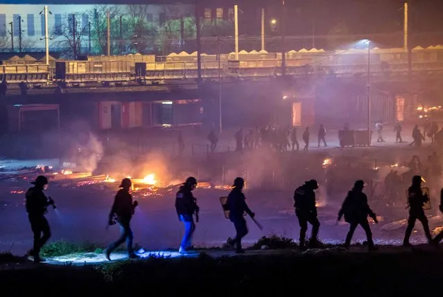 Police patrol as a huge fire blazes through the Grande- Synthe migrant camp outside the northern French city of Dunkirk late April 10, 2017, reducing it to “a heap of ashes”, the regional chief said Firefighters said at least ten people had been injured in the blaze at the camp, which was home to some 1,500 people by the end of March, living in closely- packed wooden huts. For more than a decade France' s northern coast has been a magnet for refugees and migrants trying to reach Britain, with French authorities repeatedly tearing down camps in the region. (Photo by Philippe Huguen/AFP Photo)