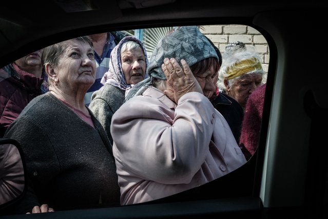 A woman covers her ears from the sound of mortar fire as people queue to collect pensions from a postal delivery van that reached the frontline despite the ongoing conflict in Mayaky, eastern Ukraine, on May 6, 2022, amid the Russian invasion of Ukraine. (Photo by Yasuyoshi Chiba/AFP Photo)