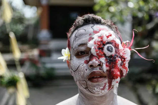 A young member of  the village community with a painted face and displaying fake wound poses before the Grebeg Ritual on June 25, 2014 in Tegallalang Village, Gianyar, Bali, Indonesia. During the biannual ritual, young members of the community parade through the village with painted faces and bodies to ward off evil spirits. (Photo by Putu Sayoga/Getty Images)