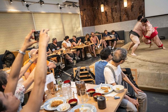 This picture taken on July 3, 2023 shows a foreign tourist (far R) wearing a costume as he tries to push a former sumo wrestler out of the ring at the Yokozuna Tonkatsu Dosukoi Tanaka restaurant in Tokyo. The restaurant opened last November, a month after pandemic-related entry restrictions were lifted, and thanks to word of mouth, it plays its sumo shows to sold-out crowds at lunch time. (Photo by Yuichi Yamazaki/AFP Photo)