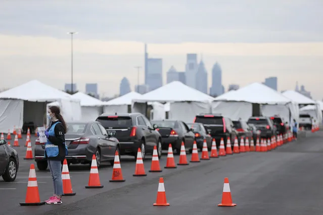 Philadelphia Medical Reserve Corps volunteer Emma Ewing, left, a sophomore at Temple University, directs cars at the city's coronavirus testing site next to Citizens Bank Park in South Philadelphia on Friday, March 20, 2020. The site, which opened Friday afternoon, is the first city-run drive-through location where people can be swabbed to determine if they have the coronavirus. At the time of opening, it was only for people with symptoms who are over 50 and healthcare workers with symptoms. (Photo by Tim Tai/The Philadelphia Inquirer via AP Photo)