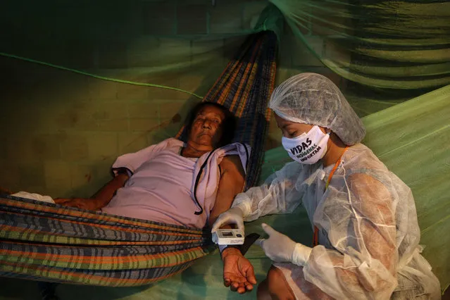 Witoto indigenous nursing assistant Vanda Ortega, 32, takes care of a patient during a healthcare visit in the Parque das Tribos, an indigenous community in the suburbs of Manaus, Amazonas State, Brazil, on May 3, 2020 during the COVID-19 novel coronavirus pandemic. Ortega goes from house to house equipped with gloves, a protective gown and a mask in which one can read: “The Life of Indigenous People Matters”, a message inspired by the slogan “Black Lives Matter” of black militants in the United States. (Photo by Ricardo Oliveira/AFP Photo)