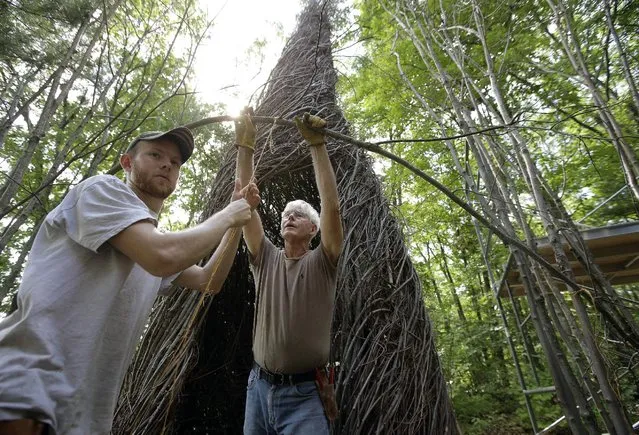 In this Wednesday, August 17, 2016 photo sculptor Patrick Dougherty, center, works with his son and assistant Sam Dougherty, left, as they construct a sculptural installation “The Wild Rumpus”, from branches and sticks on the grounds of the Tower Hill Botanic Garden, in Boylston, Mass. Dougherty’s installation opens to the public Thursday, August 25. (Photo by Steven Senne/AP Photo)