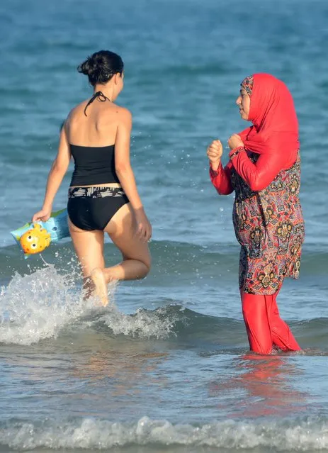 This file photo taken on August 16, 2016 shows Tunisian women, one (R) wearing a “burkini”, a full-body swimsuit designed for Muslim women, walking in the water at Ghar El Melh beach near Bizerte, north-east of the capital Tunis. The debate launched this summer in France over the Burkini is not causing such a stir in North Africa where the Islamic swimsuit is uncontroversial as the dress-code on the beaches has become increasingly prudish. (Photo by Fethi Belaid/AFP Photo)