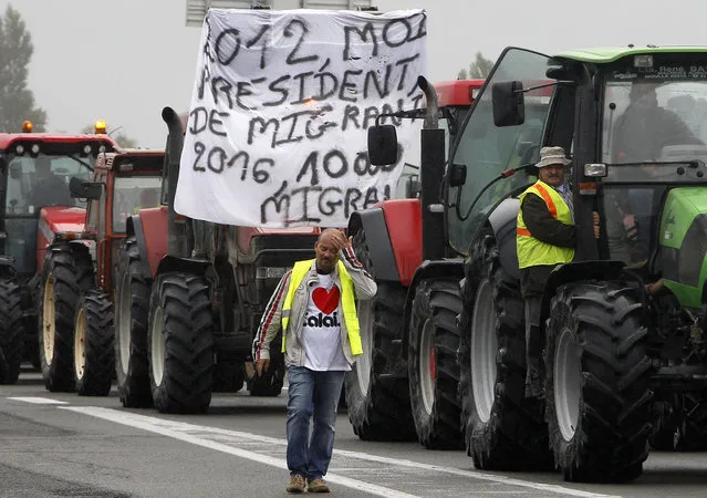A farmer walks as others drive their tractors to block the highway leading to Calais and the Channel tunnel in Calais, northern France, Monday, September 5, 2016. Hundreds of truckers in big rigs, farmers in tractors and dockers and merchants on foot blocked a major highway in northern France on Monday to demand the closure of the Calais migrant camp known as the “jungle”. Banner reads: 2012, me President, (referring to Francois Hollande), 2016, 10.000 migrants. (Photo by Michel Spingler/AP Photo)