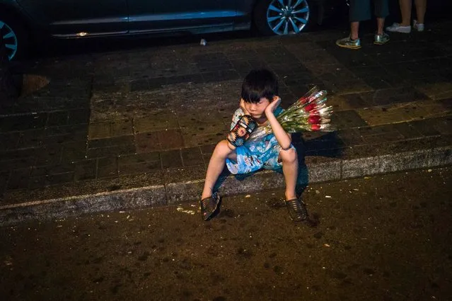 In this photo Taken on August 9, 2016, a child looks on as he sells flowers on the streets during the Qixi Festival, or Chinese Valentine's Day, in Beijing. The Qixi Festival, or Chinese Valentine's Day, falls on the seventh day of the seventh lunar month and dates back over 2,600 years and is a popular and auspicious wedding date for Chinese couples. (Photo by Fred Dufour/AFP Photo)