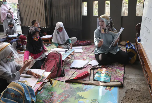 Teacher Inggit Andini, right, wearing a face shield as a precaution against the coronavirus outbreak, speaks as her students in a makeshift classroom at her residence in Tangerang, Indonesia, Monday, August 10, 2020. Andini offered free extra lessons for students who lack access to the internet as the school where she works at remain closed and switched to online learning due to the outbreak. (Photo by Tatan Syuflana/AP Photo)