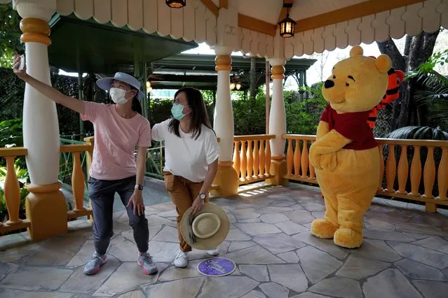 Visitors wearing face masks take a selfie with the iconic cartoon character Winnie the Pooh at the Hong Kong Disneyland, Friday, September 25, 2020. Hong Kong Disneyland reopened its doors to visitors after closed temporarily due to the coronavirus outbreak. (Photo by Kin Cheung/AP Photo)