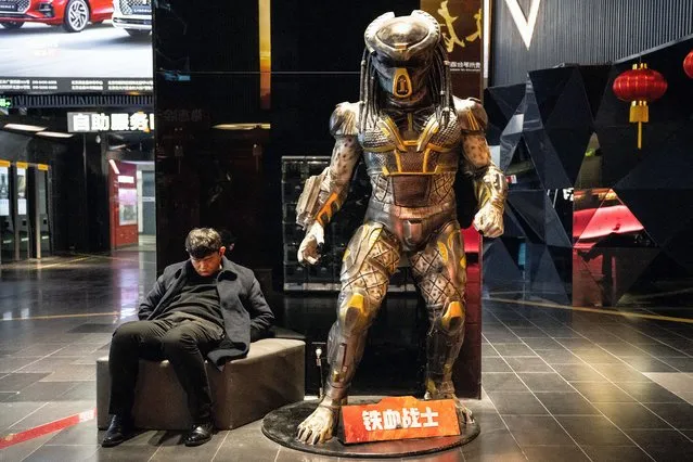 A man naps besides a life-size statue of the Predator film character at a mall in Beijing on February 6, 2023. (Photo by Noel Celis/AFP Photo)