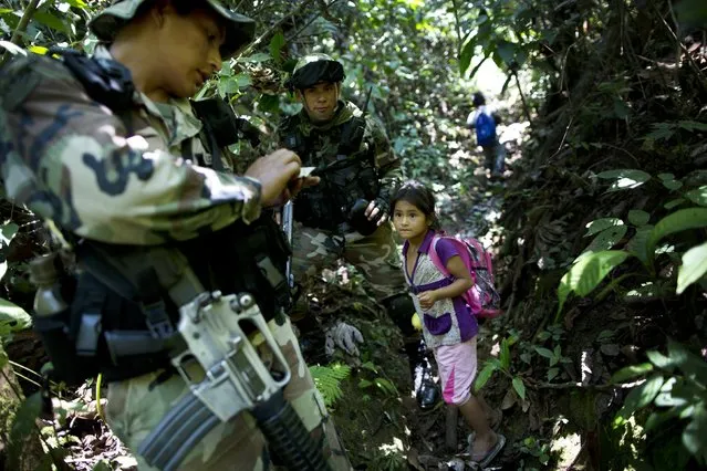 A counternarcotics special forces police officer gifts powdered milk to a girl returning from school, after the police patrol destroyed an illegal coca laboratory or maceration pond, in Tingo Maria, Peru, Monday, October 26, 2015. According to the police, most labs are simple operations where only the basic chemicals like acid, quick lime and gasoline are used to turn coca leaves into paste. The paste is later transported in 11 kilo backpacks called "costales", to another lab to be turned into cocaine. (Photo by Rodrigo Abd/AP Photo)