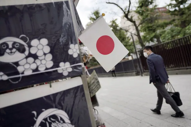 A man wearing a protective mask to help curb the spread of the coronavirus walks near a Japanese flag at a shopping arcade at Asakusa district Thursday, October 22, 2020, in Tokyo. (Photo by Eugene Hoshiko/AP Photo)