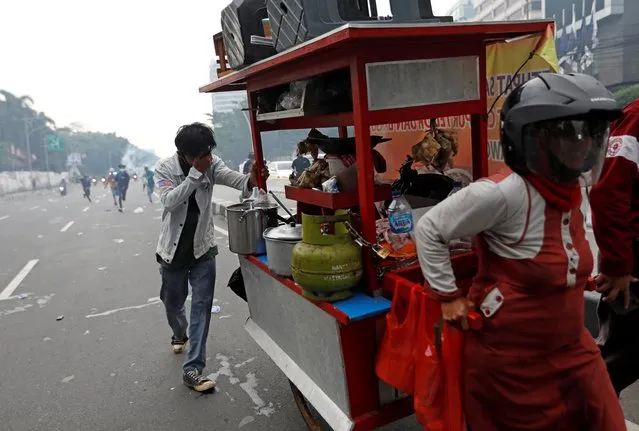 A demonstrator helps to push a food-street vendor's cart during a clash between demonstrators and police following a protest against the new so-called omnibus law, in Jakarta, Indonesia, October 13, 2020. (Photo by Willy Kurniawan/Reuters)
