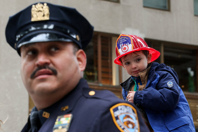 A child dressed as a New York Fire Department member watches the Veterans Day parade behind a New York Police Department officer on Fifth Avenue in Manhattan, New York City on November 11, 2025. (Photo by Kylie Cooper/Reuters)