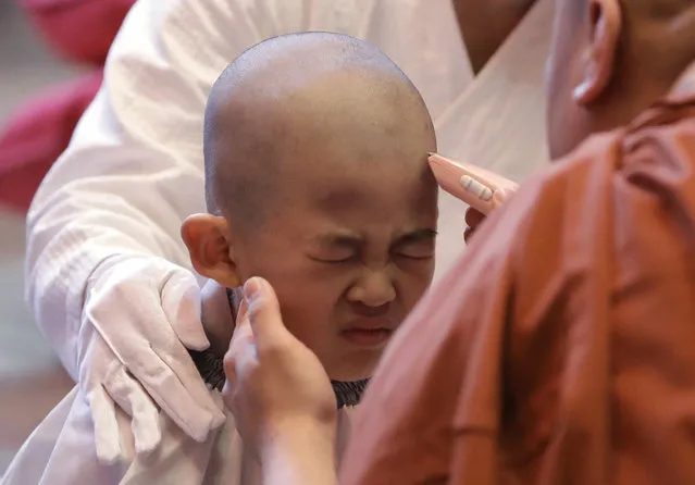 A boy reacts as a monk shaves his head during a service to have an experience of the lives of Buddhist monks, at the Jogye Temple in Seoul, South Korea, Wednesday, May 2, 2018. Ten children who entered the temple to have an experience for three weeks ahead of celebrations for Buddha's upcoming birthday on May 22. (Photo by Lee Jin-man/AP Photo)