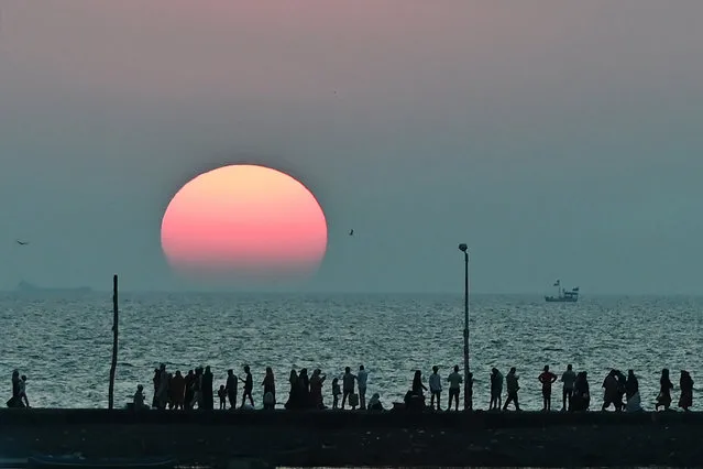 People walk along the seafront as the sun sets near Haji Ali mosque in Mumbai on November 23, 2020. (Photo by Punit Paranjpe/AFP Photo)