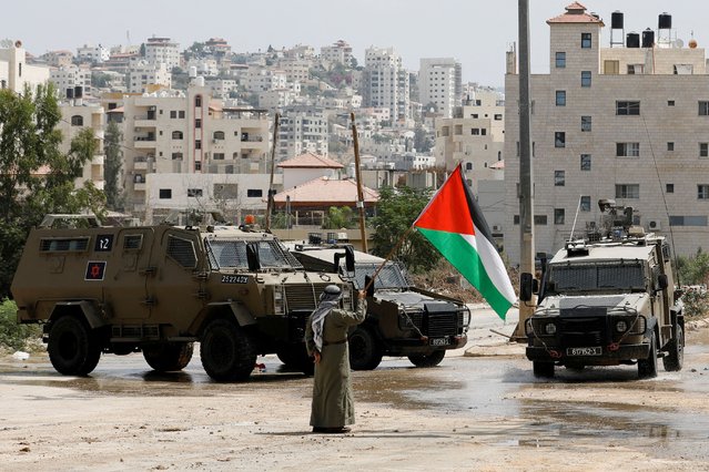 A man holds the Palestinian flag next to Israeli military vehicles during a raid in Tulkarm, in the Israeli-occupied West Bank, on August 22, 2024. (Photo by Raneen Sawafta/Reuters)