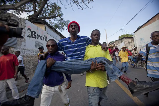 Protesters carry a man who was shot in his left leg after clashes broke out with national police during a demonstration to demand the resignation of President Michel Martelly, in Port-au-Prince, Haiti. Saturday, January 17, 2015. (Photo by Dieu Nalio Chery/AP Photo)