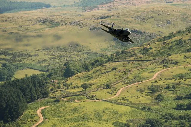 A United States Air Force (USAF) F-15 fighter jet travels at low altitude through the “Mach Loop” series of valleys near Dolgellau, north Wales on June 26, 2018. The Mach Loop valleys, situated between Dolgellau and Machynlleth, are regularly used by the military for operational low flying training which can take place as low as 76 metres from the nearest terrain. The USAF regularly use the loop to practice low-altitude flight, which confuses radar systems. The $93 million craft features a navigation pod containing a terrain-following radar which allows the jets to fly safely at very low altitudes. Its cutting-edge laser targeting system allows an enemy to be selected for destruction from a distance of 10 miles. It carries the most air-to-ground weapons of any US air force craft including Sidewinder missiles, advanced Air-to-Air Missiles and 20mm cannon with 500 rounds – used against enemy aircraft and “soft” ground targets. (Photo by Oli Scarff/AFP Photo)