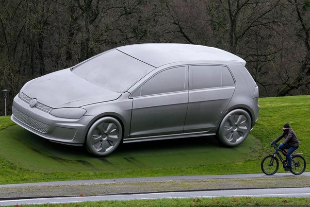 A man rides a bicycle beside a big car sculpture of a VW Golf when employees of Germany's largest carmaker went on strike at the main factory in Wolfsburg, Germany, Monday, December 9, 2024. (Photo by Martin Meissner/AP Photo)