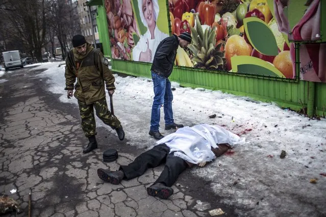 A civilian and an separatist soldier look at the body of a man after shell hit a residential area, killing two civilians in Donetsk's Kyibishevsky district, on January 29, 2015. (Photo by Manu Brabo/AFP Photo)