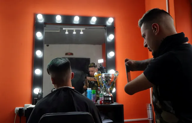 Barber Gabriel Heredia, who was born with no forearms or hands, uses his cell phone to take a photo of a customer's at his shop in Buenos Aires, Argentina, August 3, 2018. (Photo by Marcos Brindicci/Reuters)