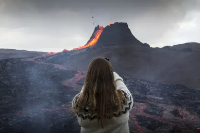A woman takes a photo as lava flows from an eruption of a volcano on the Reykjanes Peninsula in southwestern Iceland on Tuesday, March 23, 2021. Iceland's latest volcano eruption is quickly attracting crowds of people hoping to get close to the gentle lava flows. The eruption in Geldingadalur, near Iceland's capital Reykjavik, is not seen as a threat to nearby towns and the slow flows mean people can get close to action without too much harm. (Photo by Marco Di Marco/AP Photo)