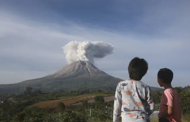 Indonesian youths watch as Mount Sinabung spews volcanic materials during an eruption in Karo, North Sumatra, Indonesia, Thursday, March 11, 2021. The volcano unleashed an avalanche of searing gas clouds flowing down its slopes during eruption on Thursday. No casualties were reported. (Photo by Binsar Bakkara/AP Photo)