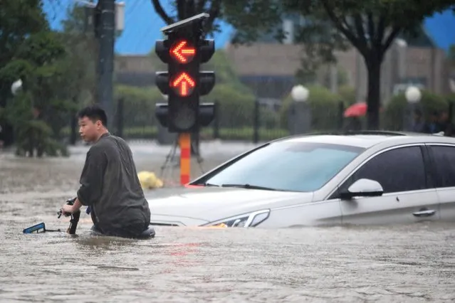 A man rides a bicycle through a flooded intersection in Zhengzhou in central China's Henan Province, Tuesday, July 20, 2021. China's military has blasted a dam to release floodwaters threatening one of its most heavily populated provinces. The operation late Tuesday night in the city of Luoyang came after several people died in severe flooding in the Henan provincial capital of Zhengzhou, where residents were trapped in the subway system and left stranded at schools, apartments and offices. (Photo by Chinatopix via AP Photo)