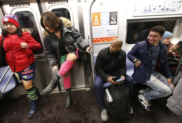Two men react as a woman puts her boots back on after removing her pants during the annual No Pants Subway Ride, Sunday, January 8, 2017, in New York. (Photo by Kathy Willens/AP Photo)