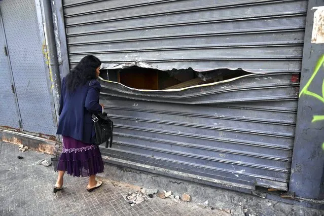 A woman peeps through the vandalised curtain of a store that was looted during protests the night before in Caracas, Venezuela on January 24, 2019. UN chief Antonio Guterres on Thursday appealed for dialogue to stop Venezuela's political crisis spiralling out of control, after opposition leader Juan Guaido declared himself interim president. (Photo by Yuri Cortéz/AFP Photo)