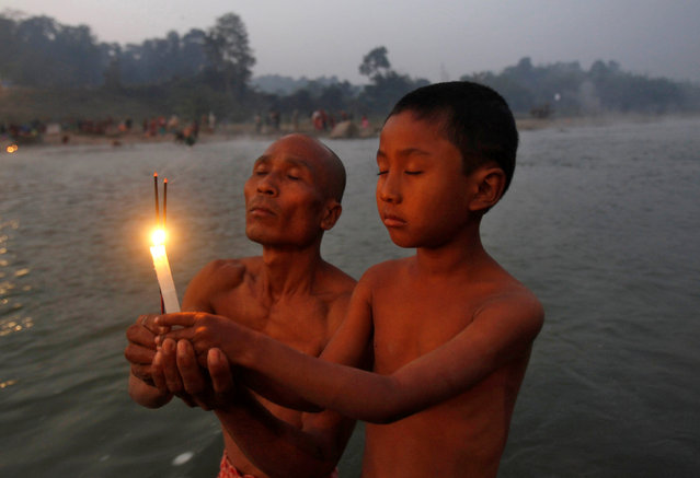 A Hindu man and his son hold burning incense sticks and a candle as they pray after taking a dip in the waters of river Howrah on the occasion of “Makar Sankranti” festival in Chakmaghat village in the northeastern state of Tripura , India, January 14, 2017. (Photo by Jayanta Dey/Reuters)