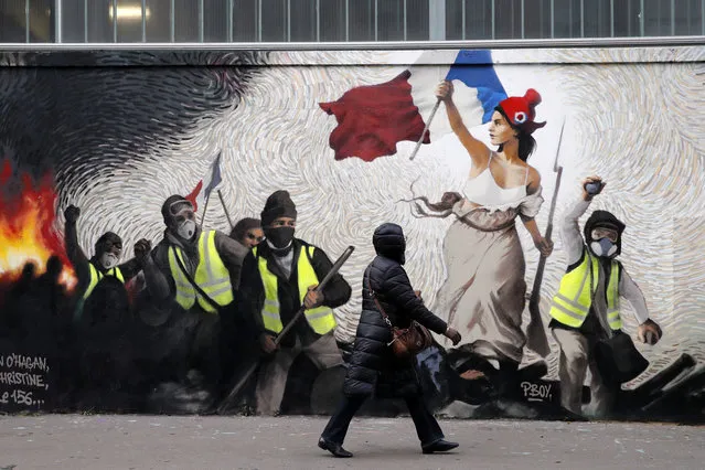 A woman passes by a mural by street artist PBOY depicting Yellow Vest (gilets jaunes) protestors inspired by a painting by Eugene Delacroix, “La Liberte guidant le Peuple” (Liberty Leading the People), in Paris, Thursday, January 10, 2019. French President Emmanuel Macron is facing a mountain of challenges in the new year starting with yellow vest protesters who are back in the streets to show their anger against high taxes and his pro-business policies that they see as favoring the wealthy rather than the working class. (Photo by Christophe Ena/AP Photo)