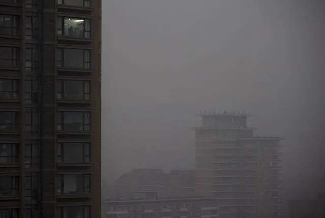 People are seen inside a residential apartment building as city skyline shrouded with heavy haze in Beijing Wednesday, February 26, 2014. Beijing remained cloaked in hazardous white pollution hiding much of its skyline Wednesday, despite the announced closures or production cuts at 147 of the city's industrial plants. (Photo by Andy Wong/AP Photo)