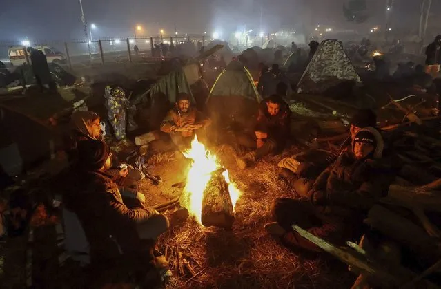 Migrants warm themselves near a fire as they gather at the checkpoint "Kuznitsa" at the Belarus-Poland border near Grodno, Belarus, on Wednesday, November 17, 2021. Some of the migrants have children with them at the border in their desperate bid to reach the EU. Most are fleeing conflict, poverty and instability in the Middle East and elsewhere. (Photo by Maxim Guchek/BelTA via AP Photo)