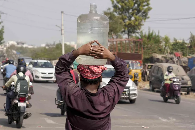 A man carries water on his head and walks through a busy street in Hyderabad, India, Thursday, March 7, 2024. (Photo by Mahesh Kumar A./AP Photo)