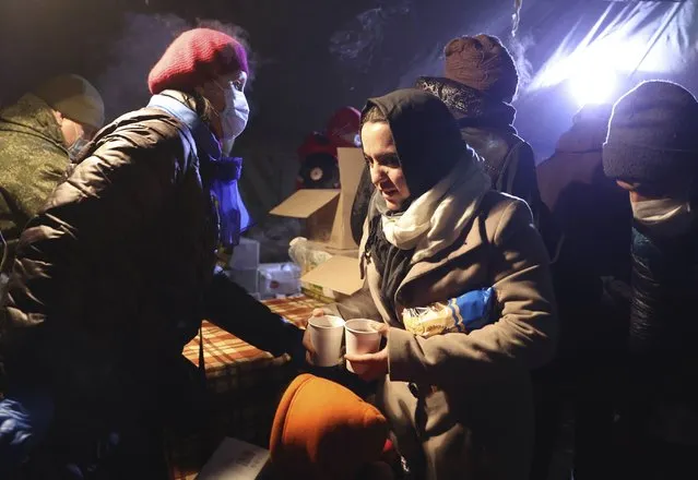 Migrants get a meal in the logistics center of the checkpoint “Bruzgi” at the Belarus-Poland border near Grodno, Belarus, Wednesday, December 1, 2021. The West has accused Belarusian President Alexander Lukashenko of luring thousands of migrants to Belarus with the promise of help to get to Western Europe to use them as pawns to destabilize the 27-nation European Union in retaliation for its sanctions on his authoritarian government. Belarus denies engineering the crisis. (Photo by Oksana Manchuk/BelTA via AP Photo)