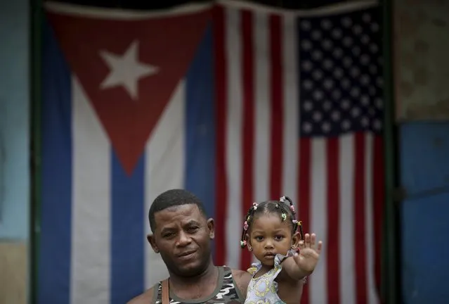 Yoendry Gainsa, 35, a bricklayer, holds his daughter while posing for a photograph in front of the Cuban and U.S. flags in Havana, March 25, 2016. Regarding Obama's historic visit to the island, Gainsa said “I hope everything gets better and that there will be better work and development for our children. Long live Obama”. (Photo by Ueslei Marcelino/Reuters)