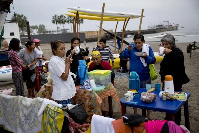 In this May 15, 2015 photo, swimmers eat breakfast on Fishermen's Beach in the Pacific Ocean in Lima, Peru. The swimmers bought their breakfast from a vendor selling “health food” after their therapeutic swimming session. (Photo by Rodrigo Abd/AP Photo)