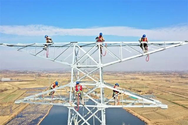 Electricians work on a transmission tower at the construction site of a new 220 kv high-voltage transmission and transformation project on January 3, 2022 in Quanjiao County, Chuzhou City, Anhui Province of China. (Photo by Song Weixing/VCG via Getty Images)