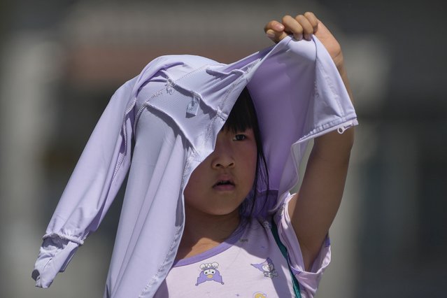 A child uses a sun protection clothing to shield from the sun as she walks along a street during an unseasonably hot day in Beijing, Monday, June 17, 2024. (Photo by Andy Wong/AP Photo)