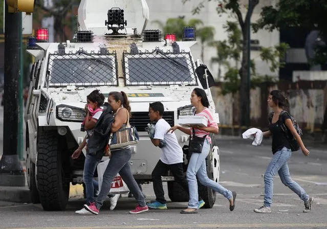 People cover their faces from teargas as they walk past an armored car of the National Guard in Caracas, Venezuela, Wednesday, May 3, 2017. Driving the latest outrage is a decree by Venezuelan President Nicolas Maduro to begin the process of rewriting Venezuela's constitution, which was pushed through in 1999 by his predecessor and mentor, the late President Hugo Chavez. (Photo by Ariana Cubillos/AP Photo)