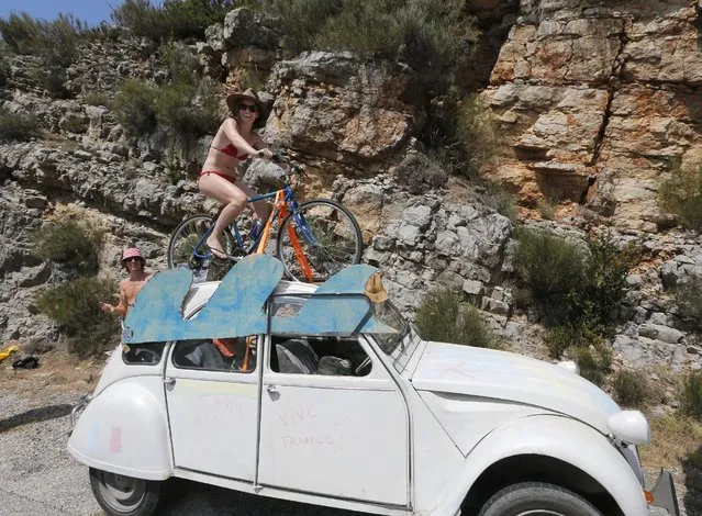 A spectator sits on a bicycle mounted on top of a French Citroen 2CV classic car as she waits for the pack to pass during the seventeenth stage of the Tour de France cycling race over 161 kilometers (100 miles) with start in Digne-les-Bains and finish in Pra Loup, France, Wednesday, July 22, 2015. (Photo by Christophe Ena/AP Photo)