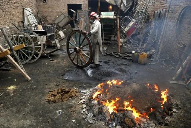 A worker burns waste rubber and cow dung cakes for heat as he repairs wheels for carts pulled by livestock in Peshawar, Pakistan, January 18, 2016. (Photo by Khuram Parvez/Reuters)