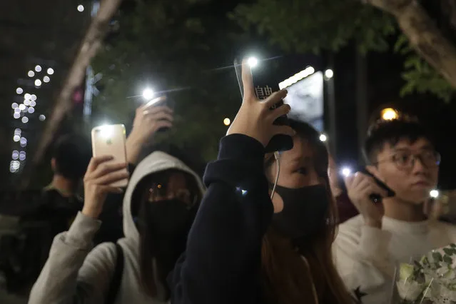 Attendees hold up their lit mobile phones to mark the six months anniversary memorial for a man who fell to his death while hanging a protest banner against an extradition bill, in Hong Kong Sunday, December 15, 2019 in Hong Kong. (Photo by Mark Schiefelbein/AP Photo)