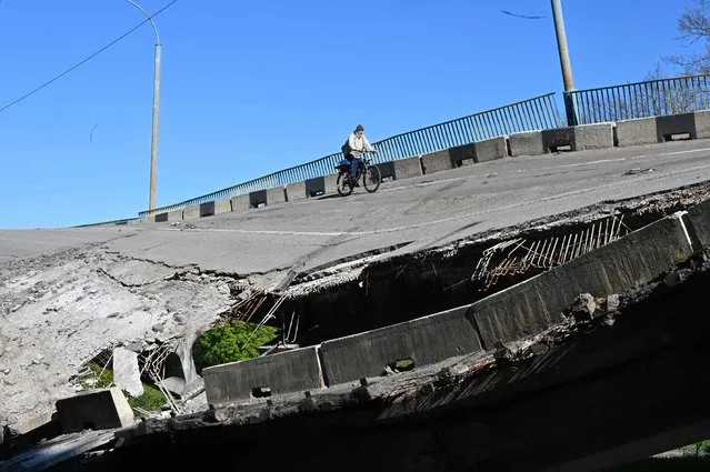 A man rides his bicycle over a heavily damaged bridge near Pechenegi village in the Kharkiv region on May 5, 2022, amid the Russian invasion of Ukraine. (Photo by Sergey Bobok/AFP Photo)